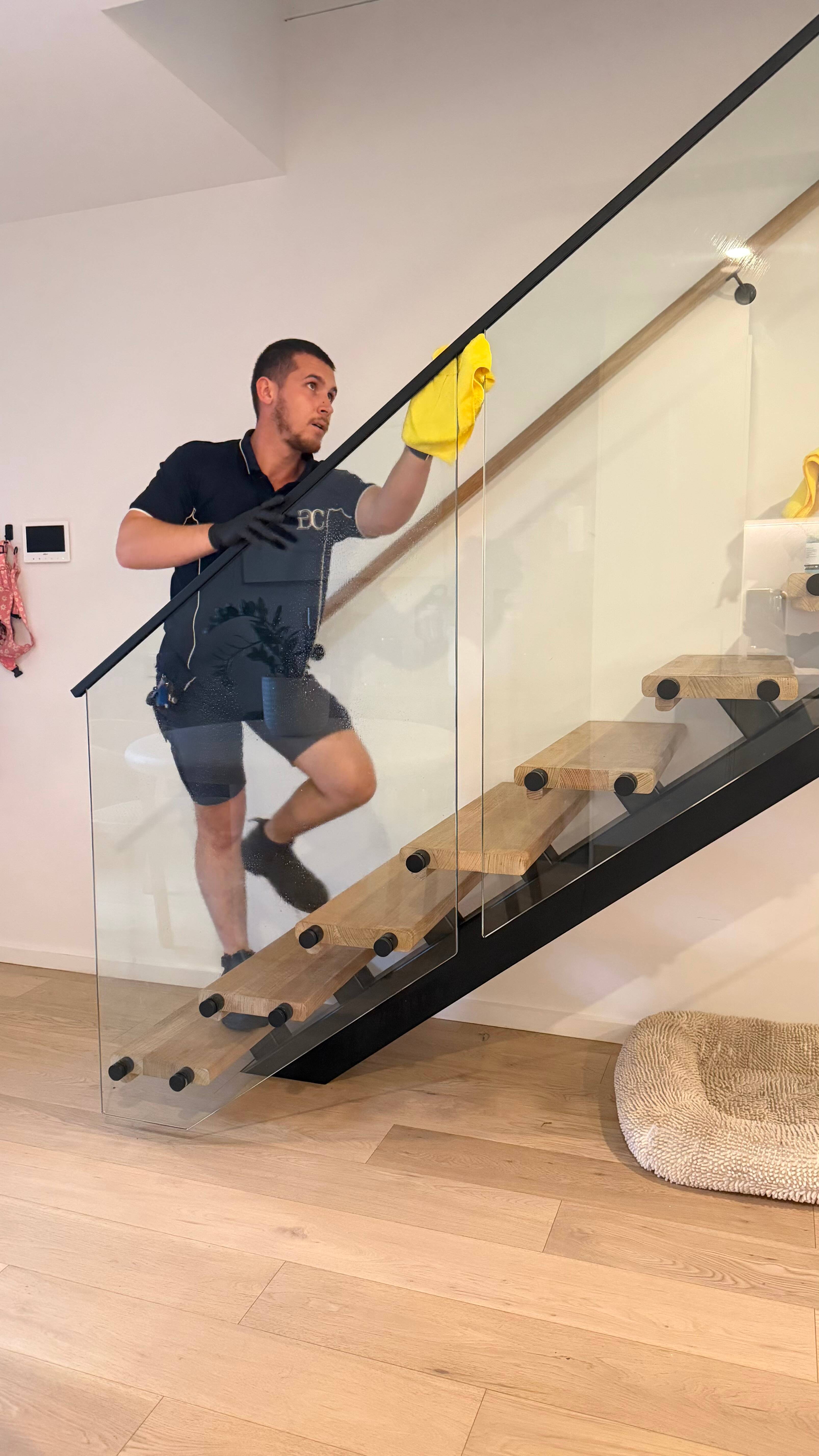 Gleam Clean Co. cleaner wiping down a glass staircase balustrade in a Canberra home